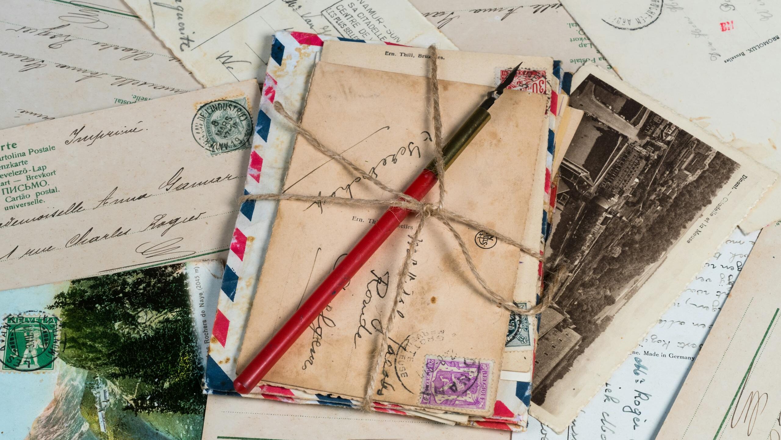 a collection of vintage postcards and envelopes tied with twine featuring a pen and old stamps. 1906606 scaled e1734112539535